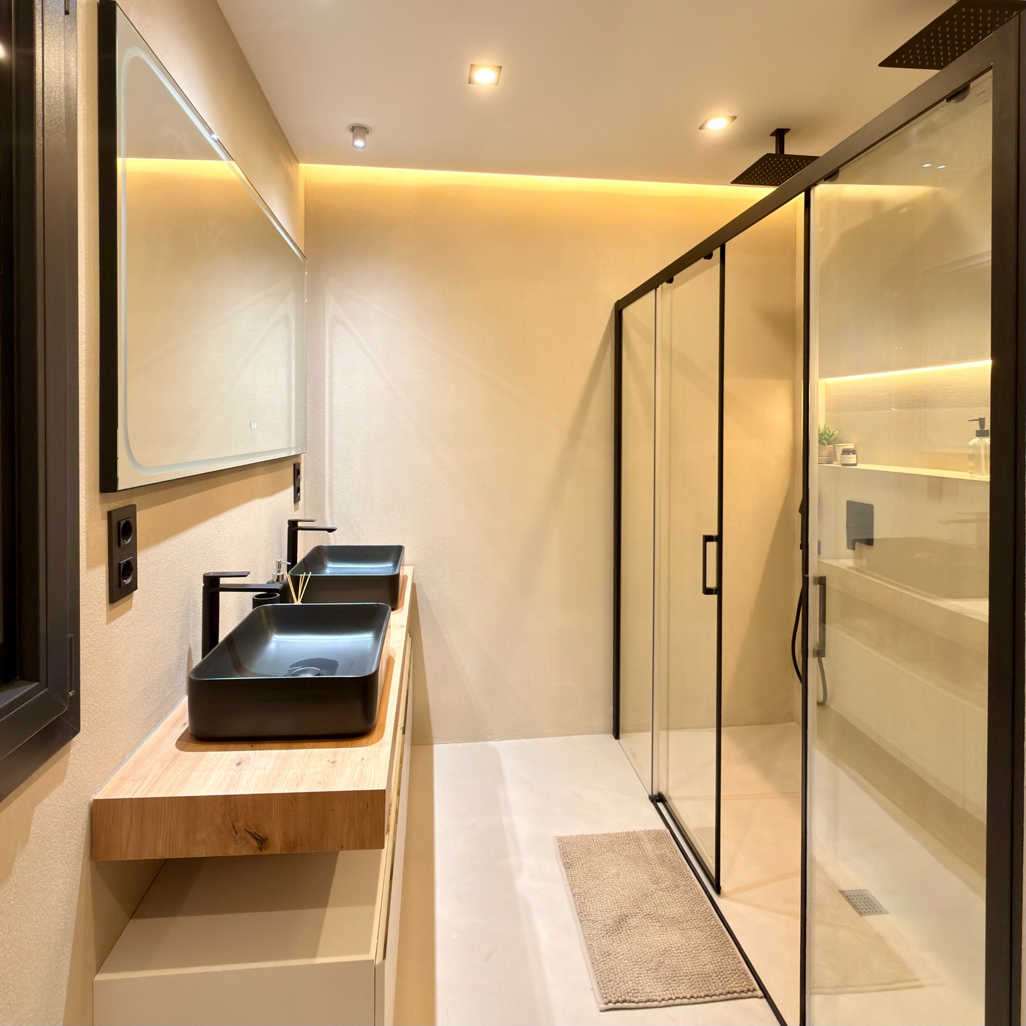 Baño con doble lavabo negro, mueble de madera y ducha acristalada