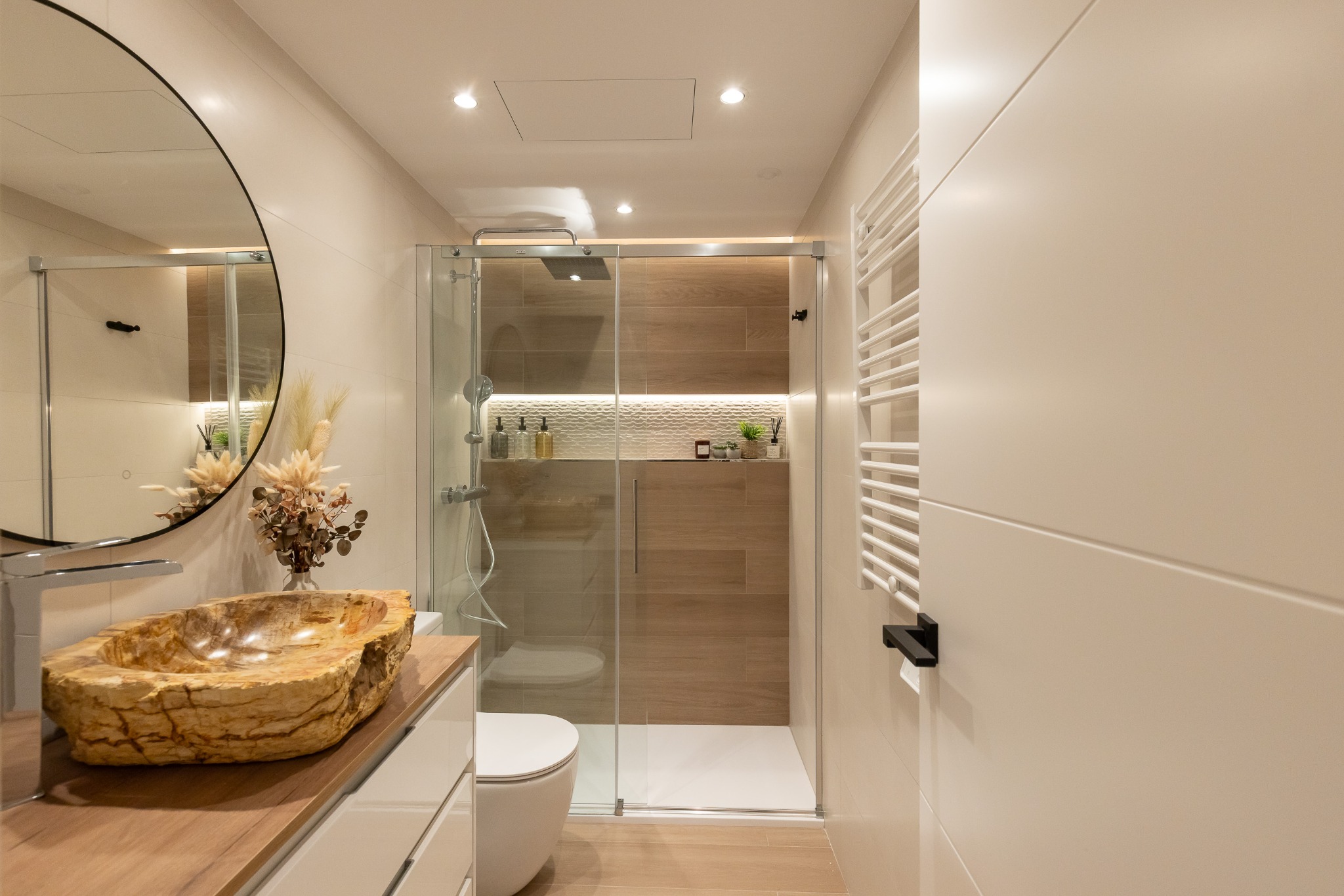 Baño con lavabo de acabado pétreo, espejo circular y ducha